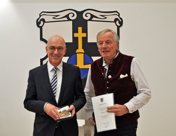 Das Foto zeigt den Bürgermeister und Ferdinand Koll vor dem Wappen der Stadt Meckenheim im Ratssaal.