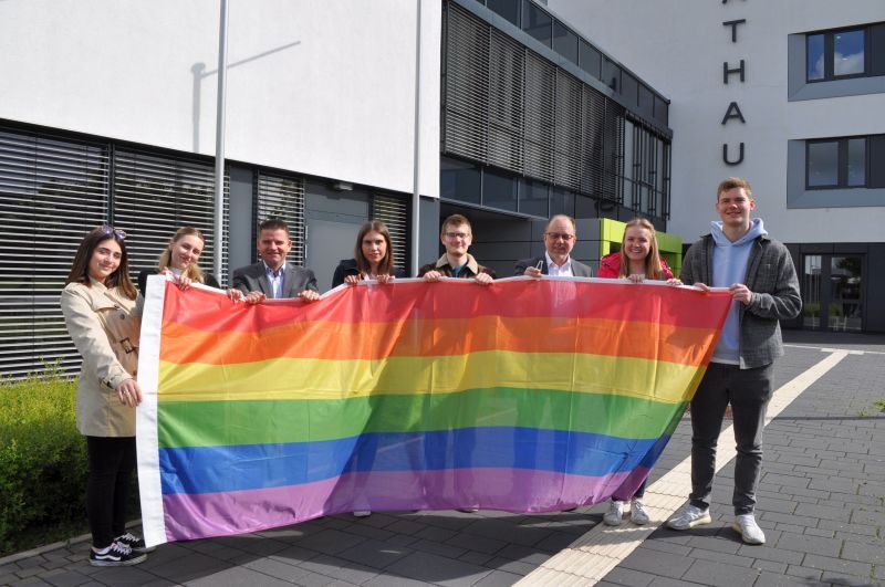 Foto zeigt den Bürgermeister, Technischen Beigeordneten und Auszubildende der Stadt Meckenheim mit der Regenbogenflagge vor dem Rathaus.