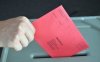 Foto zeigt eine Hand, die einen Wahlbrief in die Wahlurne wirft