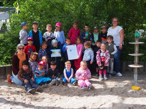 Foto zeigte die Kita-Kinder und Erzieherinnen auf dem Außengelände der Kita Steinbüchel mit der Auszeichnung.
