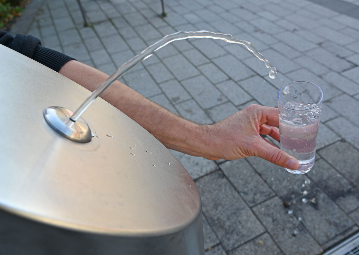 Wasser aus dem Brunnen fließt in ein Glas, das von einer Hand gehalten wird.