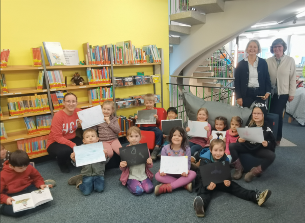 Kinder der Kita Blütentraum sitzen auf dem Boden und halten die Bilder in der Hand.