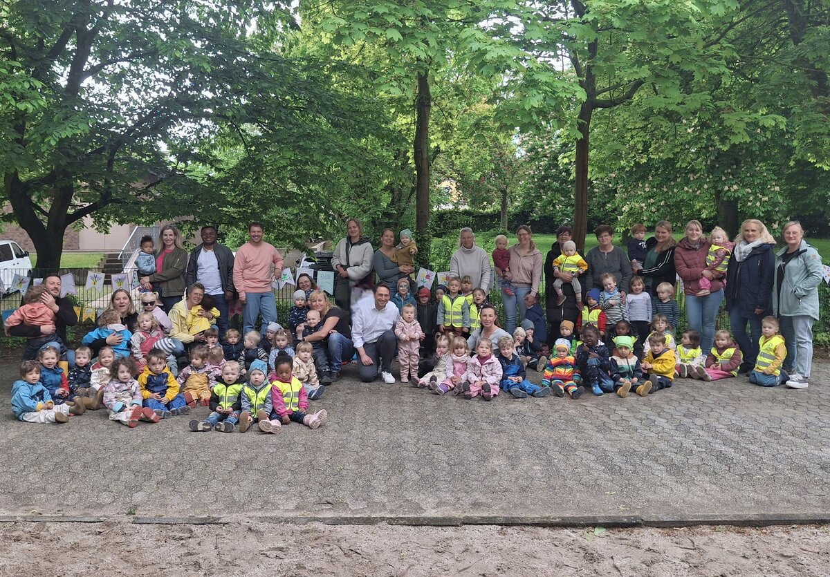 Alle Beteiligten stehen für ein Gruppenfoto zusammen vor dem Zaun des Wasserspielplatzes.