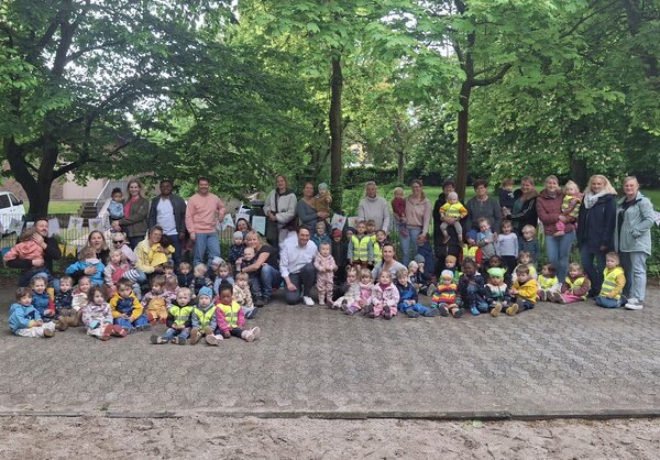 Alle Beteiligten stehen für ein Gruppenfoto zusammen vor dem Zaun des Wasserspielplatzes.