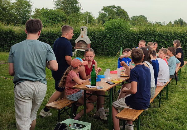 Alle sitzen am langen Tisch draußen zusammen und stärken sich bei Pizza und Getränken.