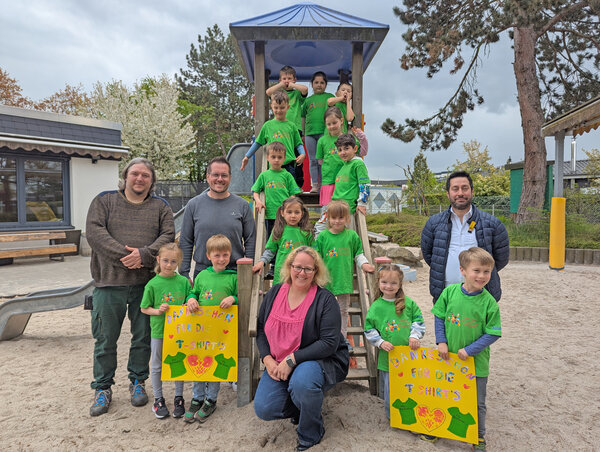 Die Beteiligten der Übergabe stehen und knien auf dem Spielplatz an der Rutsche.