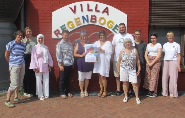 Die Beteiligten stehen außen vor dem Schriftzug "Villa Regenbogen" der Kita.