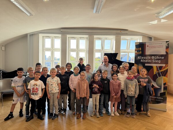 Bild vergr&ouml;&szlig;ern: Schülerinnen und Schüler der Klassen 3a, 3b und 3c mit Pianist Markus Kreul und Kirsten Felgner von der Kreissparkassenstiftung für den Rhein-Sieg-Kreis nach dem musikalischen Erlebnis „Zauberkasten Klavier“