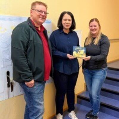 Die Organisatoren des Martinszuges, Julia und Andreas Grohs, überreichen eines der Bilderbücher an Kathrin Merzenich (Mitte), Leiterin der Kita "Zur Glocke"